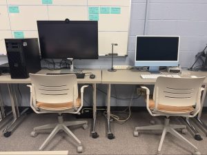 A long table against a wall with a PC computer, Mac computer, and various peripherals.
